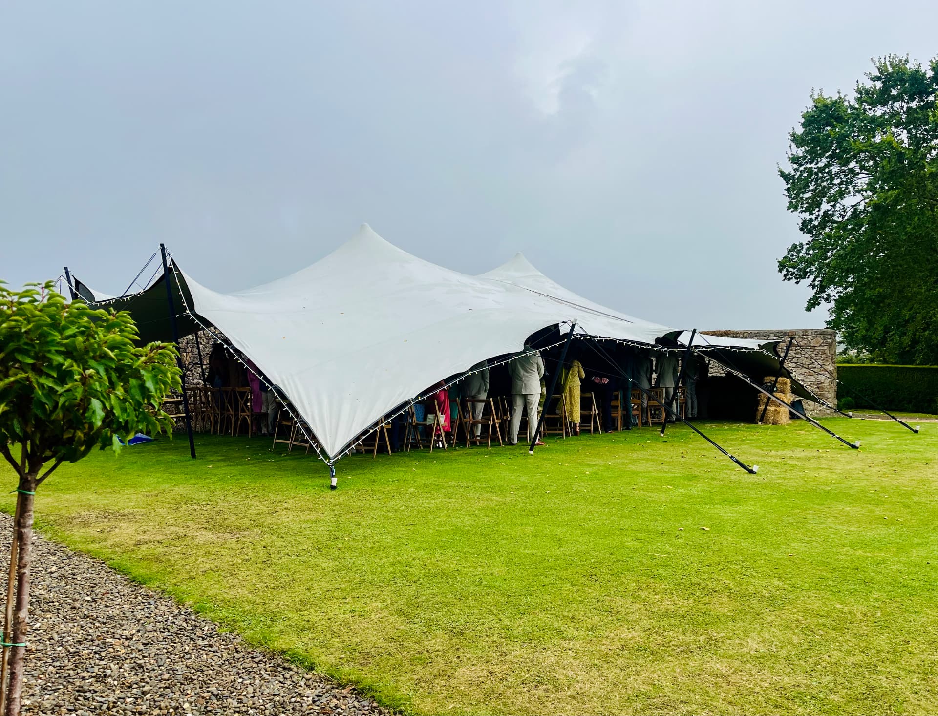 Guests gathered beneath a Gecko Events stretch tent on a lawn, with string lights along the edge of the canvas