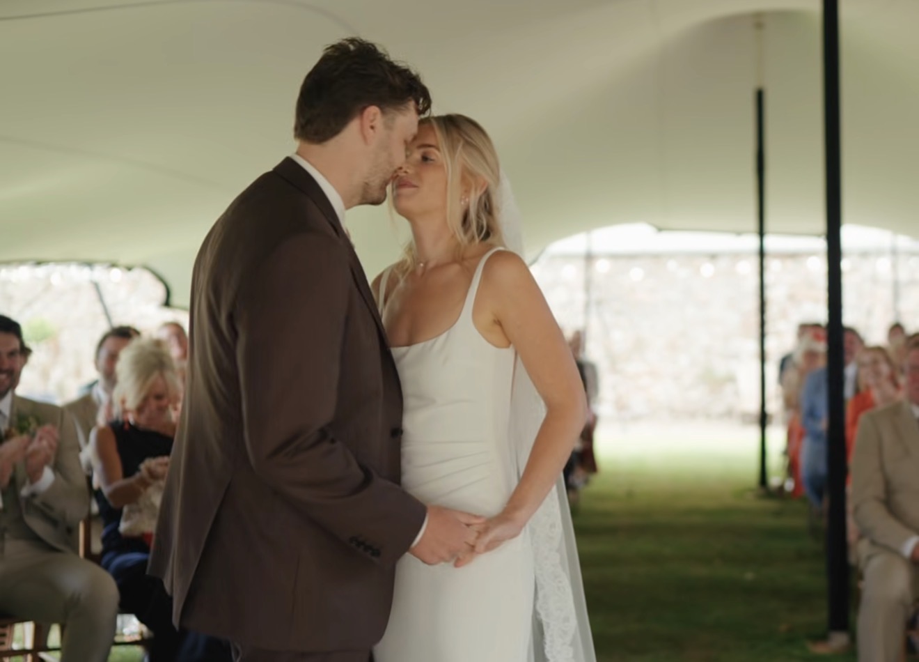 Wedding ceremony beneath a canopy tent with guests seated either side