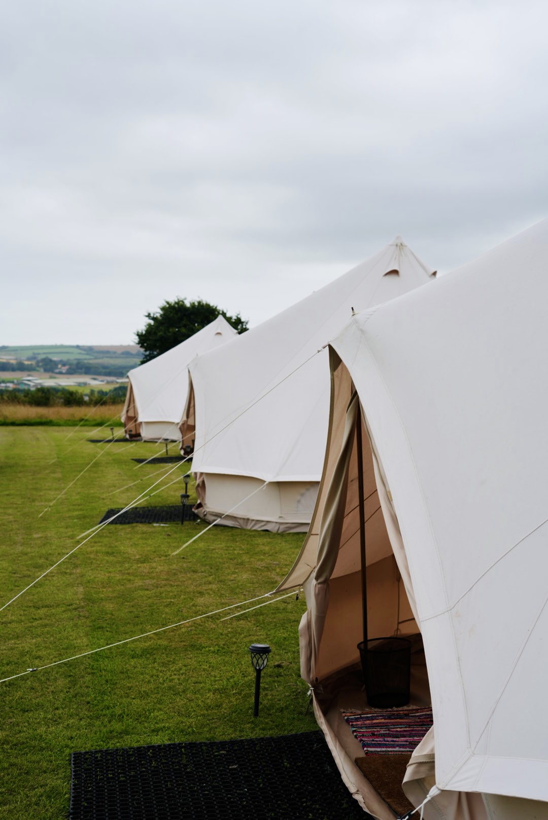 Line of white bell tents pitched on a grassy field overlooking rolling countryside
