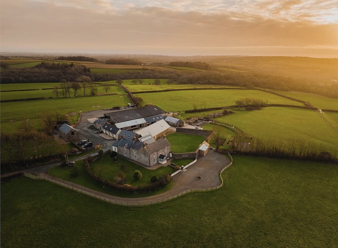 Aerial view of a stone farmhouse and barns among rolling green fields at golden hour