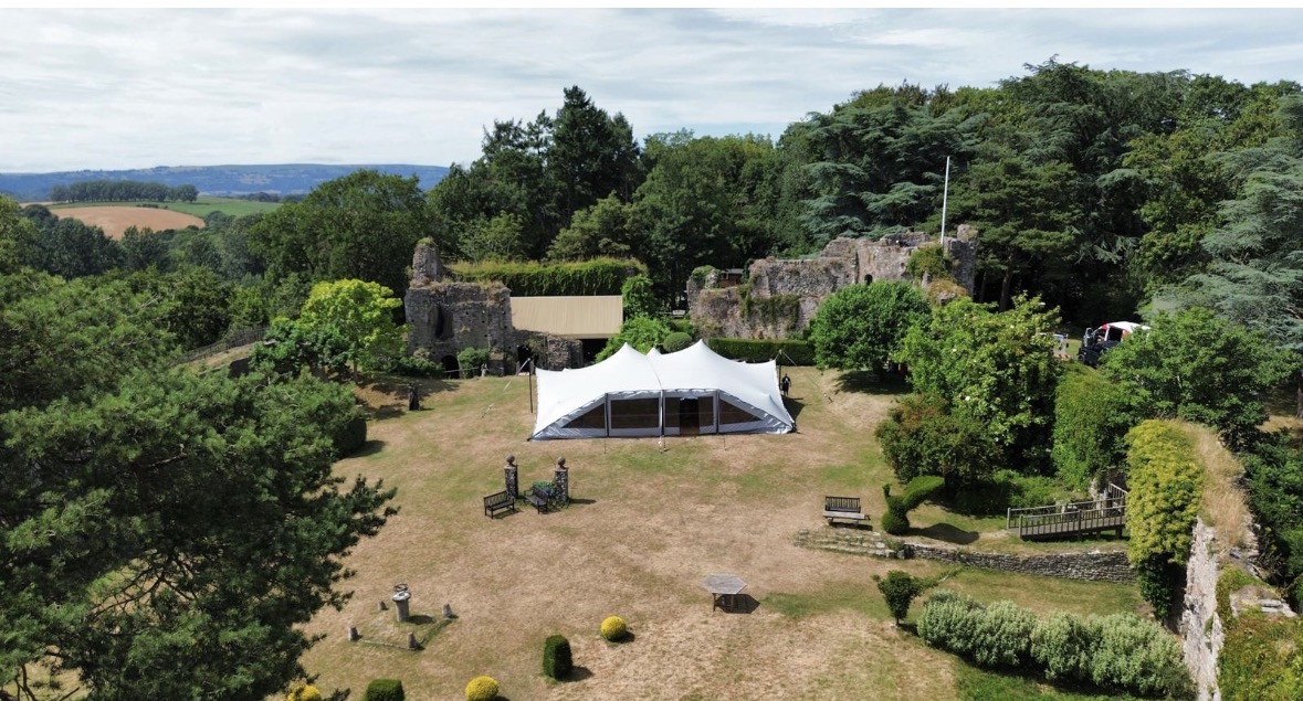 Aerial view of a white marquee on a lawn beside stone castle ruins